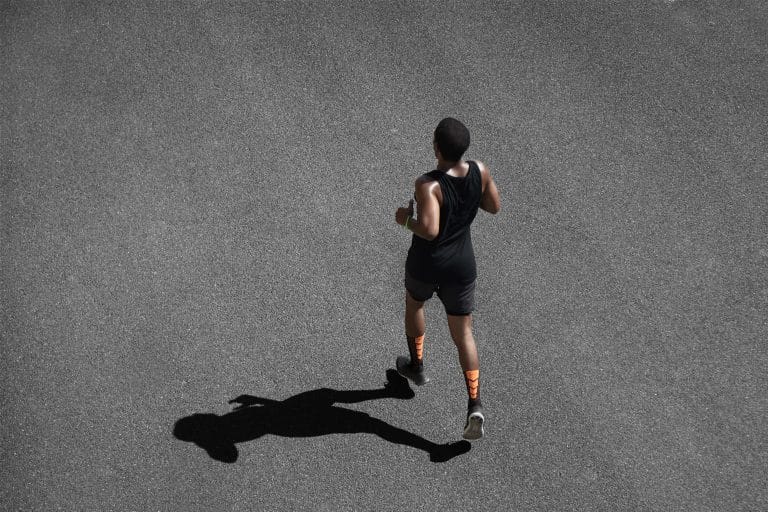 Top view of African runner wearing black sportswear training on black pavement at central position. Muscular fit sport model exercising sprint on city road
